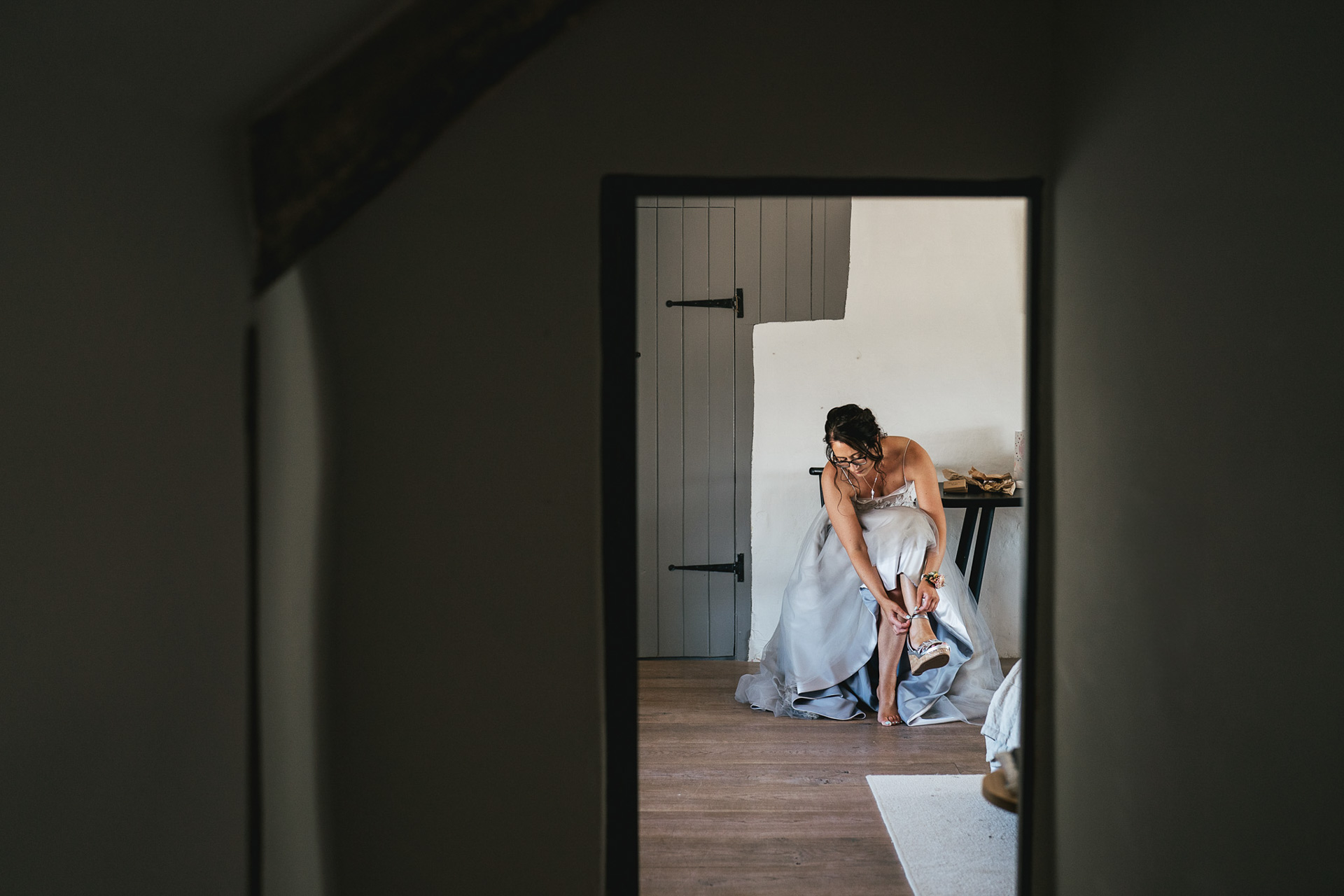 A bride getting ready for a wedding, and putting on her shoes in the farmhouse at River Cottage in Devon