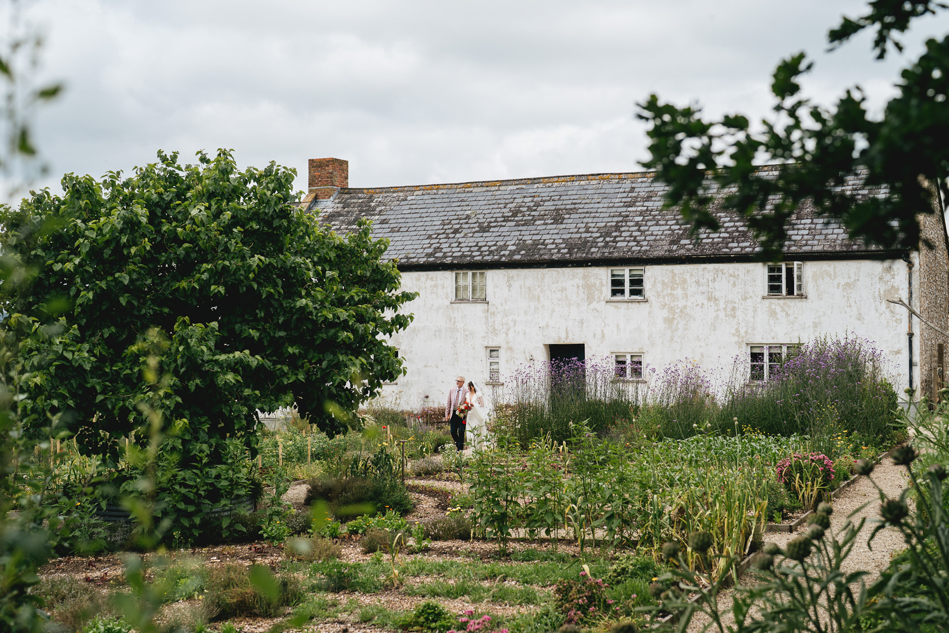 A bride and her father walking through the kitchen garden at River Cottage for her outdoor wedding ceremony