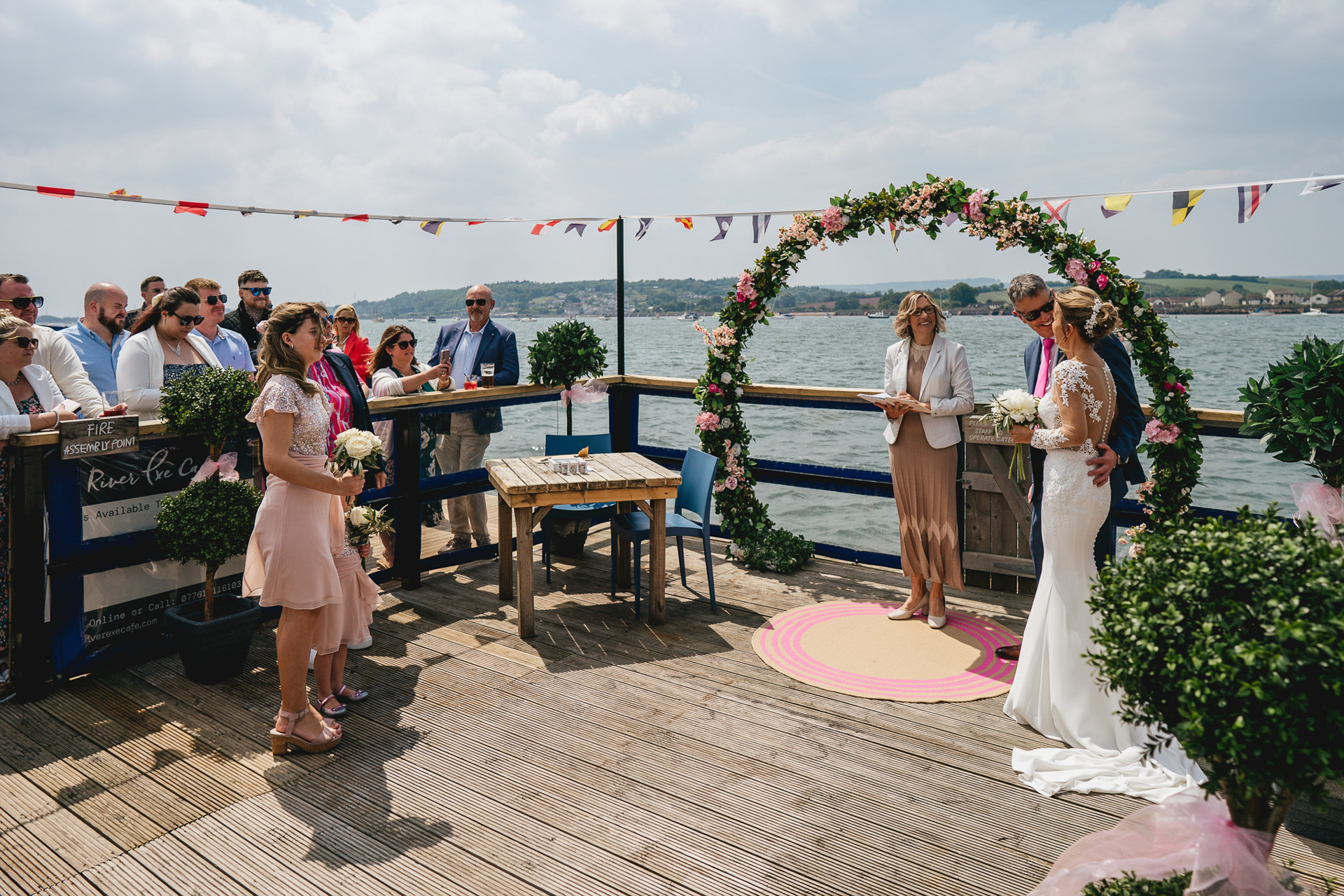 An outdoor wedding ceremony on the River Exe Cafe floating boat, with the river behind