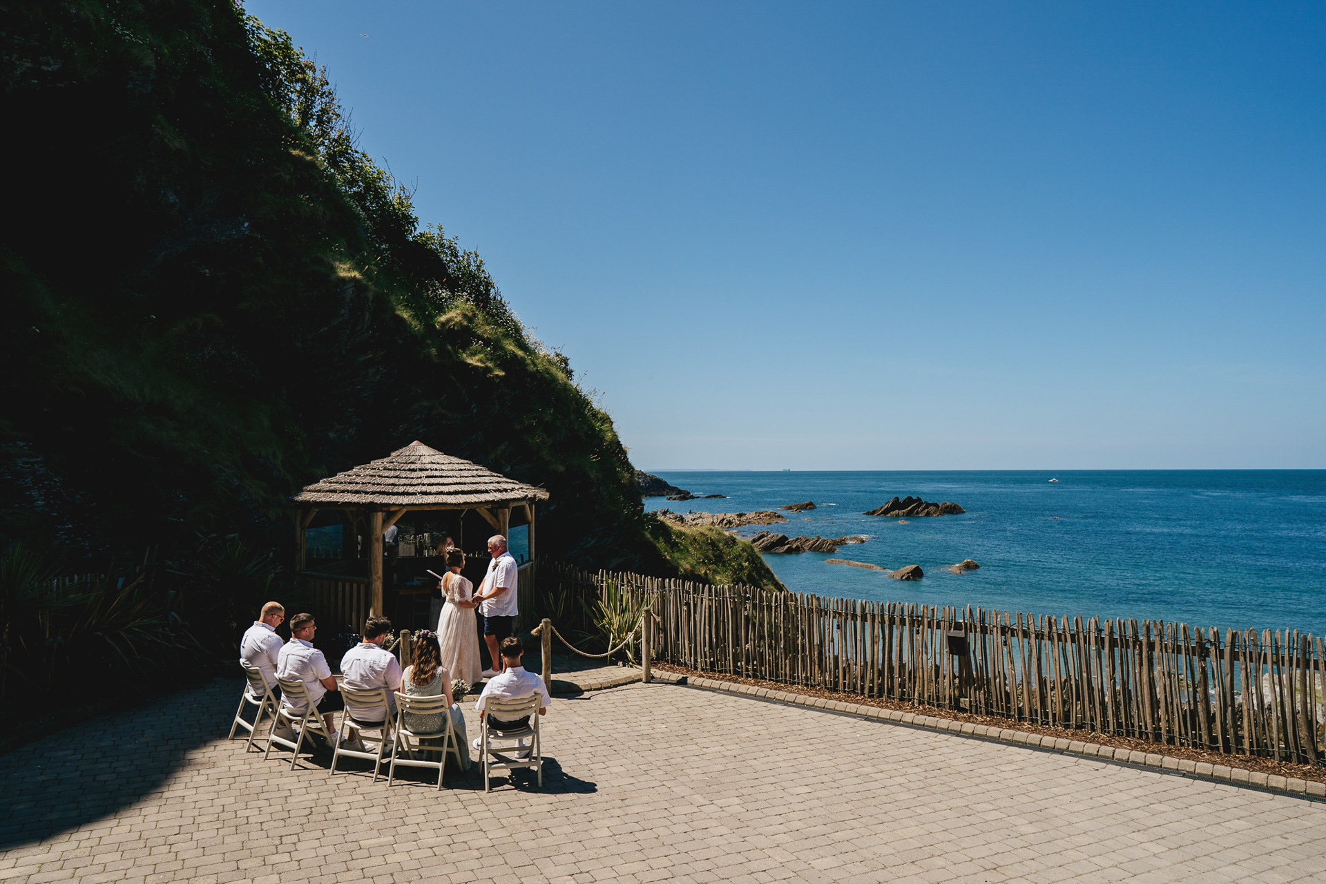 A tiny elopement wedding ceremony at Tunnels Beaches in Devon, with blue skies and sea behind