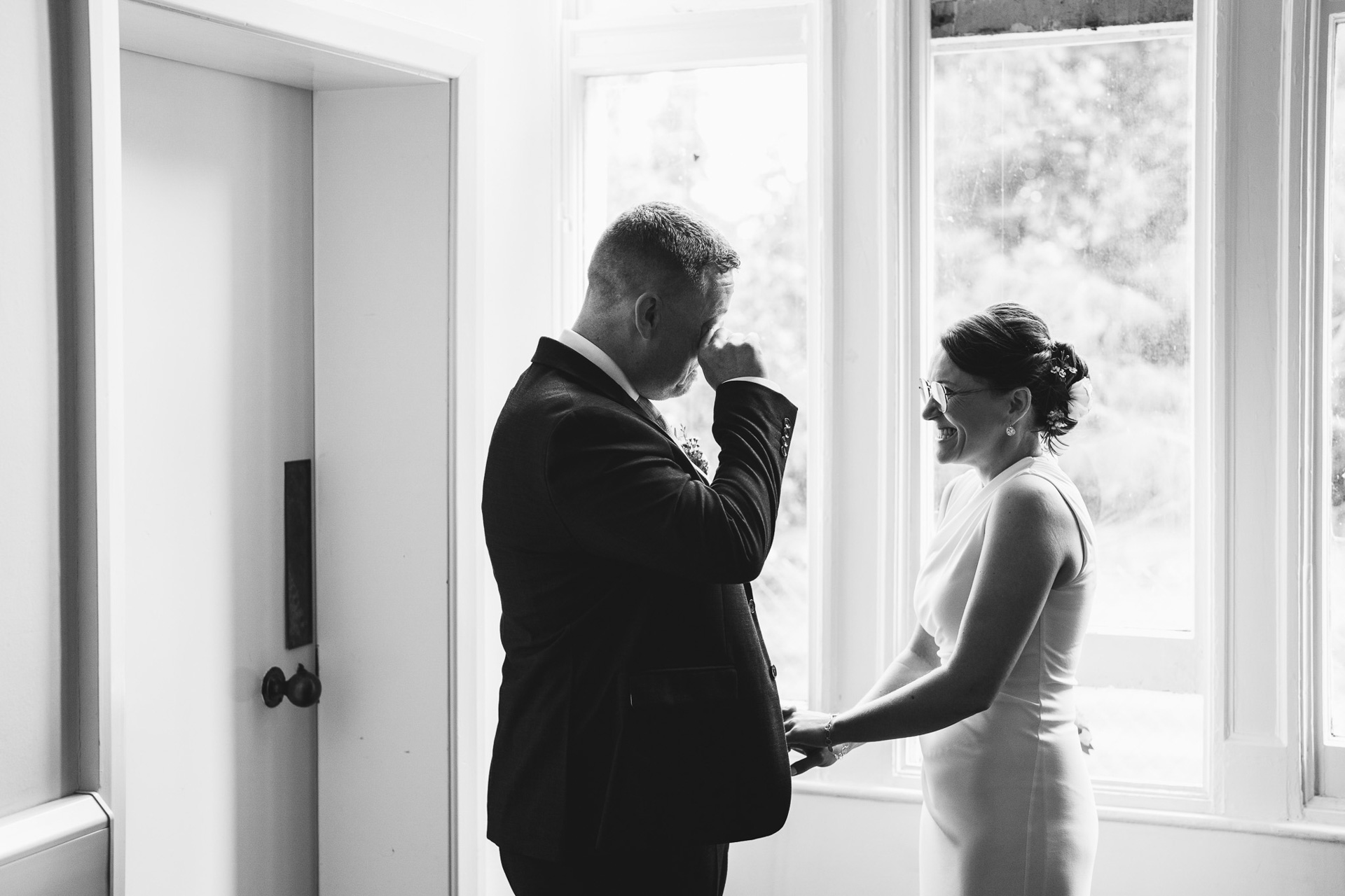 A couple getting married at Larkbeare House in Exeter, with the groom wiping a tear from his eye and the bride smiling at him