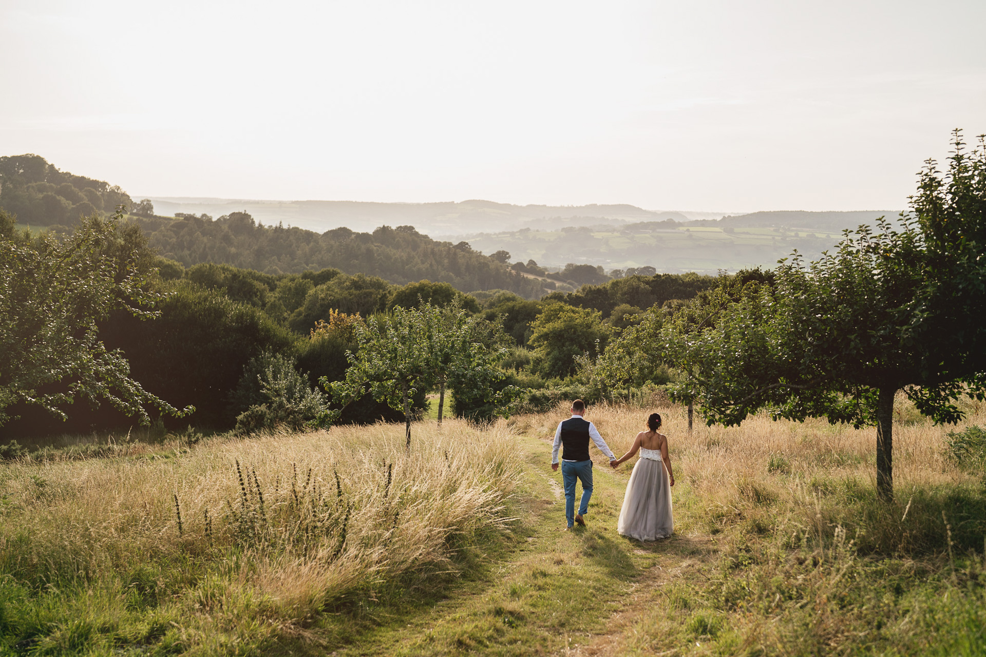 A couple walking hand in hand with Devon views behind them on their River Cottage wedding day