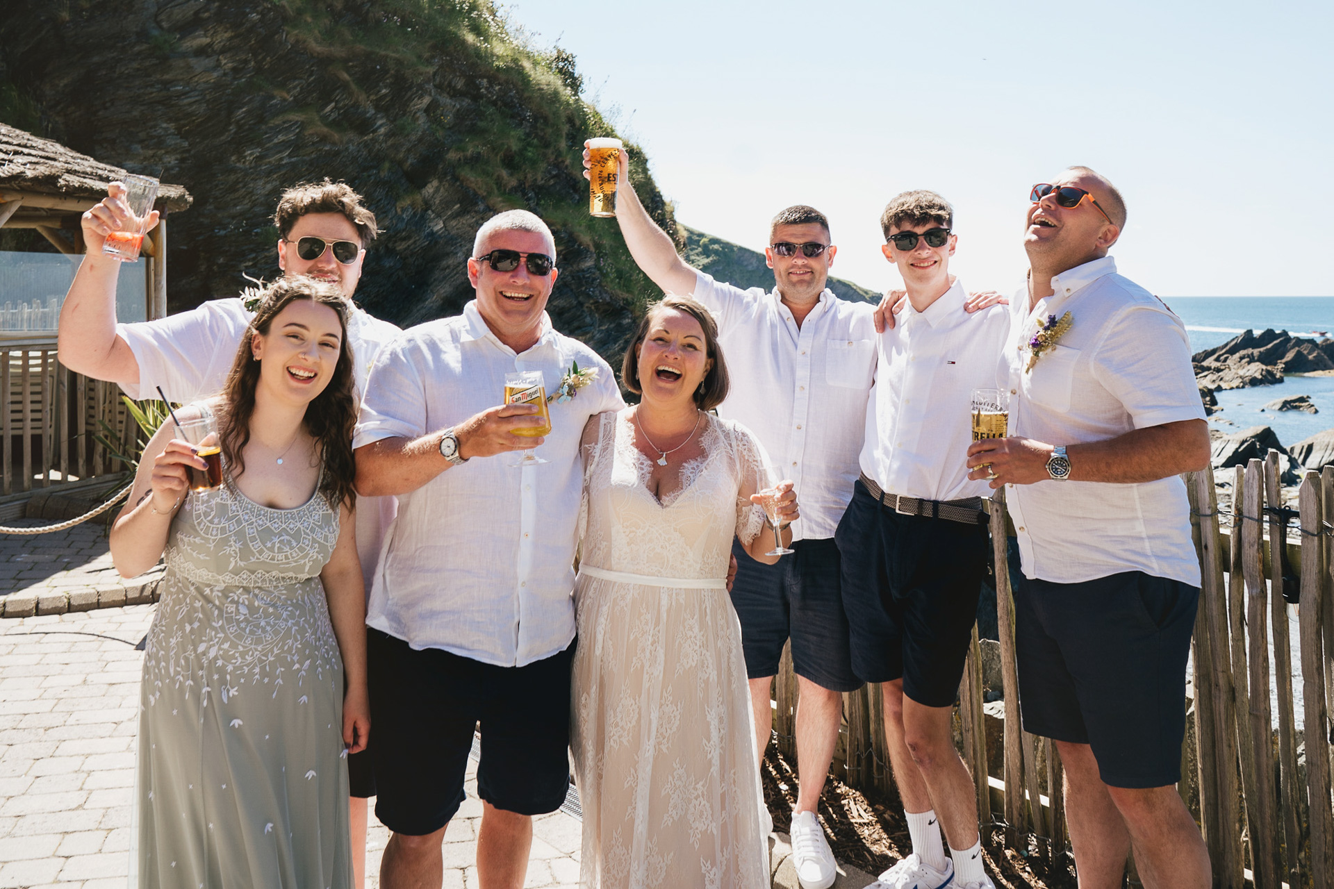 A bride and groom with family all raising glasses and smiling at the camera in a relaxed group wedding photo at Tunnels Beaches 