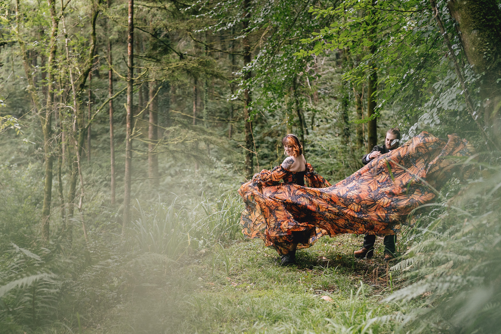 A bride with an incredible orange patterned wedding dress with a huge train, twirling and showing it off in some woodland