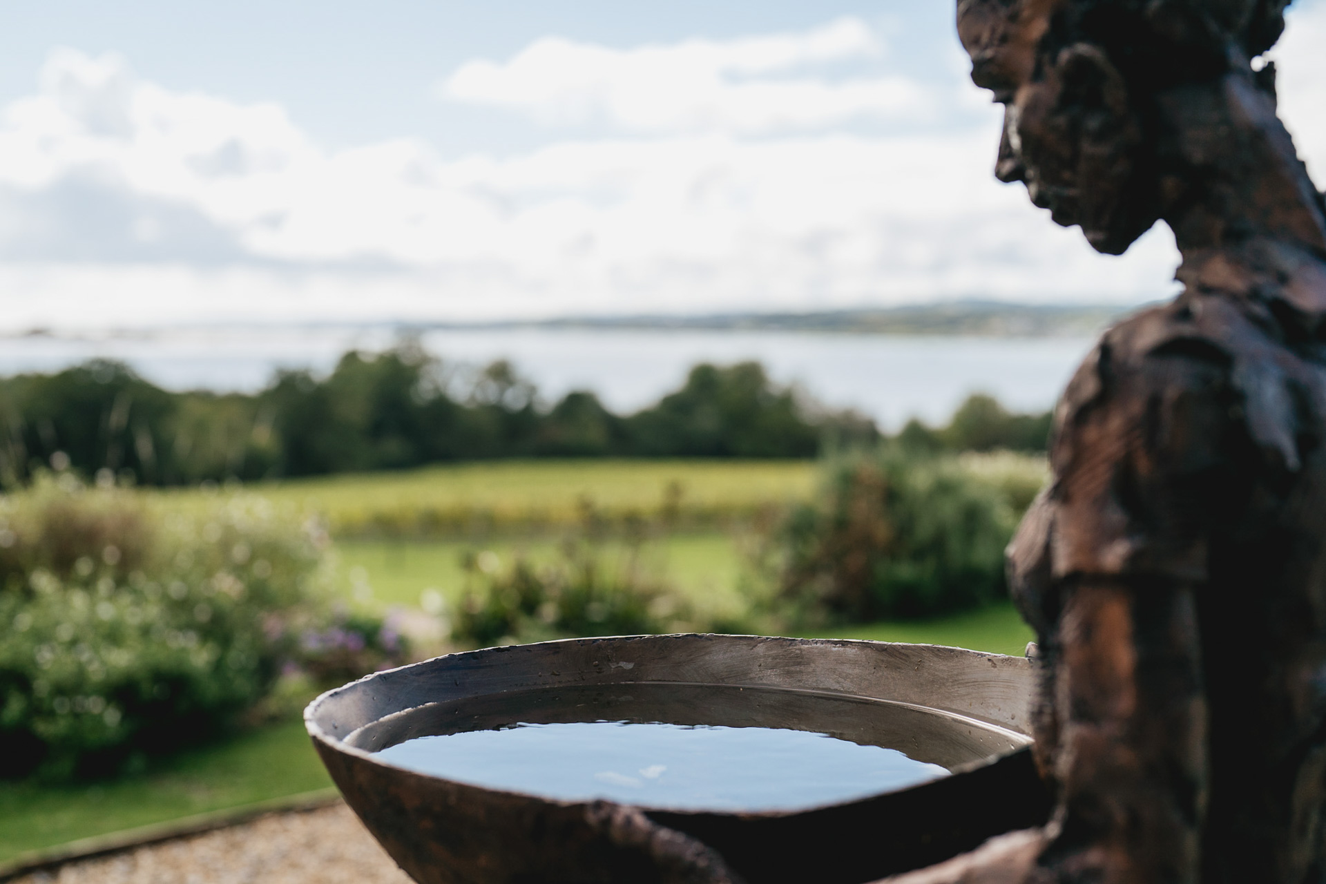 A sculpture at Lympstone Manor in Devon, reflecting the sky in a bowl of water, with views of the Exe Estuary behind 