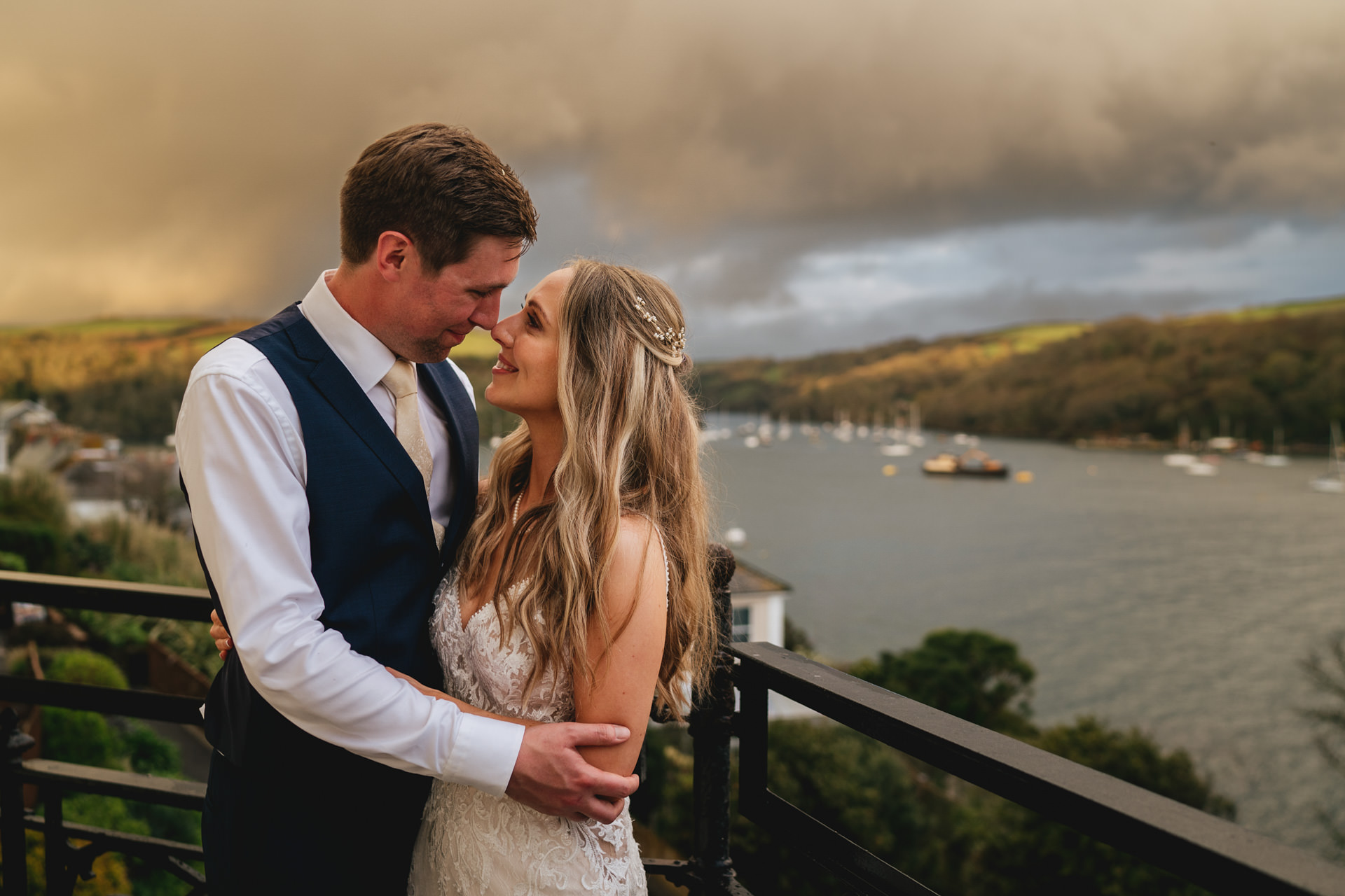 A bride and groom smiling at each other with the River Fowey behind them at their Cornwall wedding