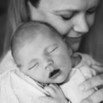 A mother smiling gently with her newborn baby sleeping on her shoulder