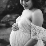 Maternity portrait of a pregnant woman, with a white dress and her hands cradling her bump.