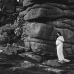 A maternity portrait of a woman standing outside on Dartmoor Devon by a tor, with her hands on her pregnant stomach