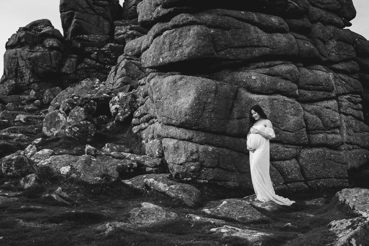 A maternity portrait of a woman standing outside on Dartmoor Devon by a tor, with her hands on her pregnant stomach