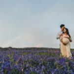 A maternity photo with a couple standing in a field of bluebells, cuddling together with their hands on her pregnant stomach