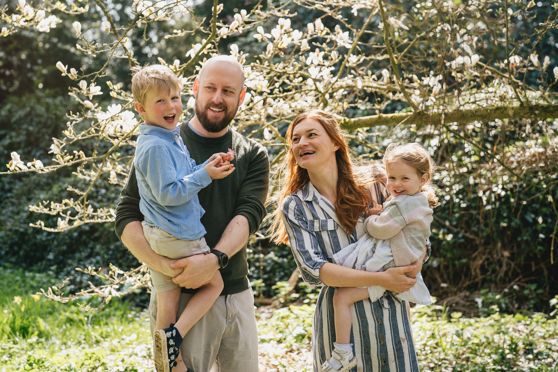 A family group photo with parents holding children under a magnolia in full bloom at an arboretum near Exeter in Devon 