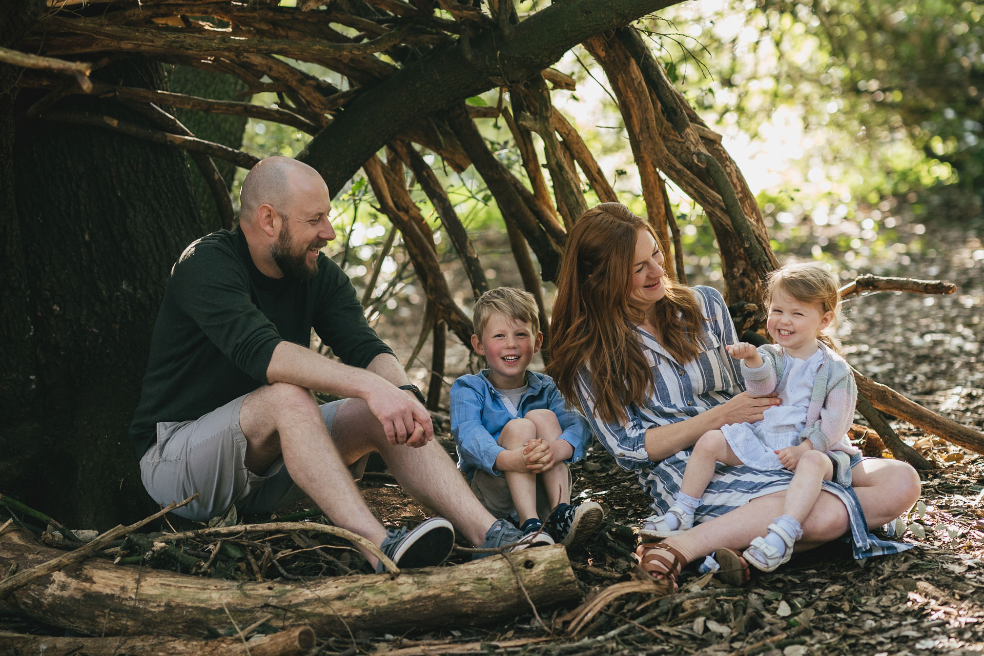 A family sitting together in a den in woodland near Exeter, during a photography session with Helen Lisk