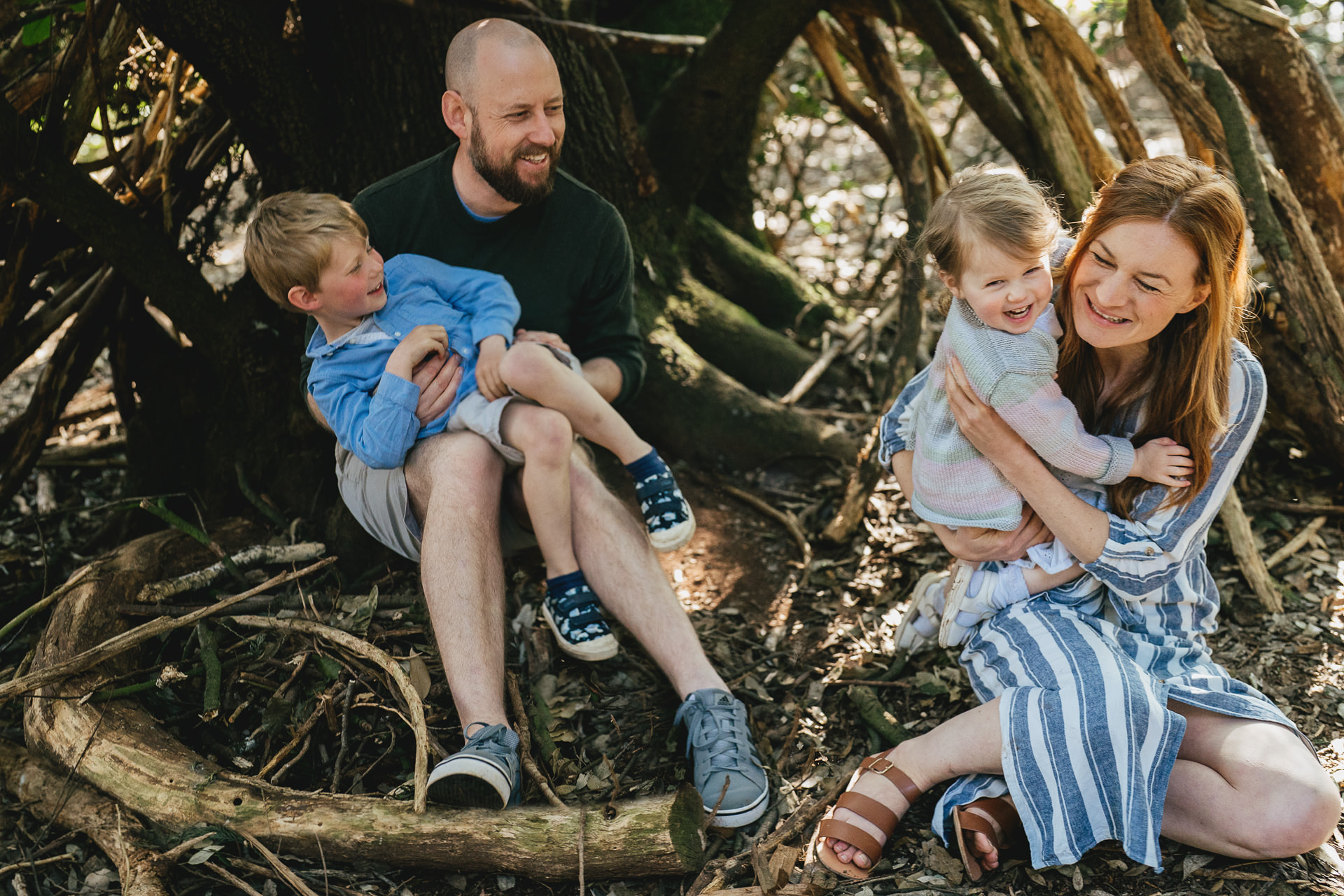 A family sitting together in a den in woodland near Exeter, during a family photography session