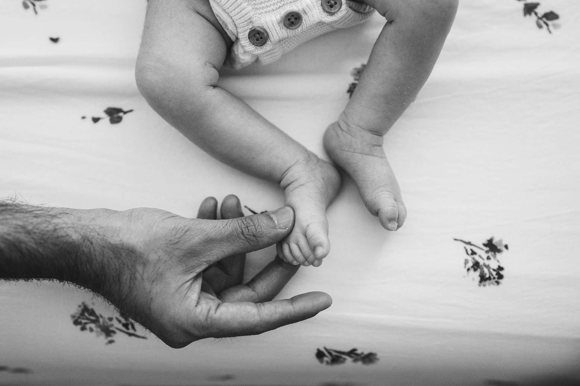 A father's hand holding a newborn baby's foot