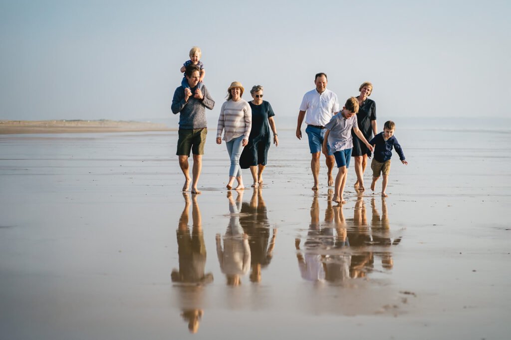 A group having a family photography session on the beach in Devon, with evening sunlight and reflections on the wet sand