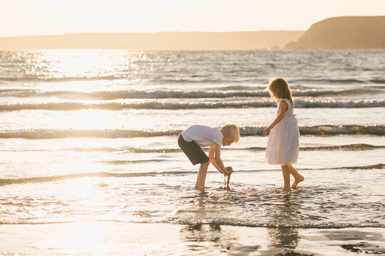 Two siblings playing together on a beach with the sun setting behind them during an evening family photography session