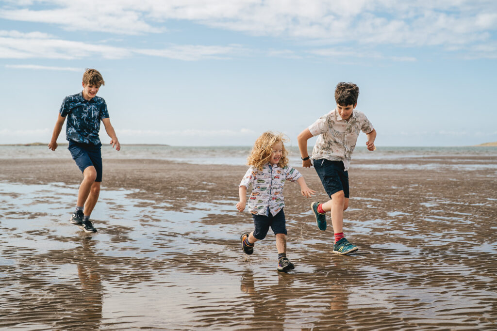 Three boys running together across sand during a family photography session in Devon