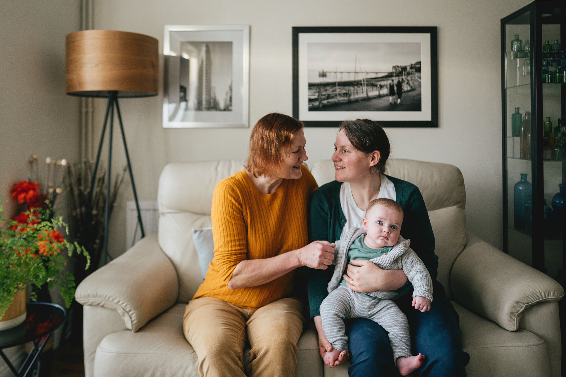Parents sitting together at home with their baby son, smiling at each other on the sofa