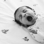 A newborn baby lying on a bed and yawning during a photo shoot at home in London