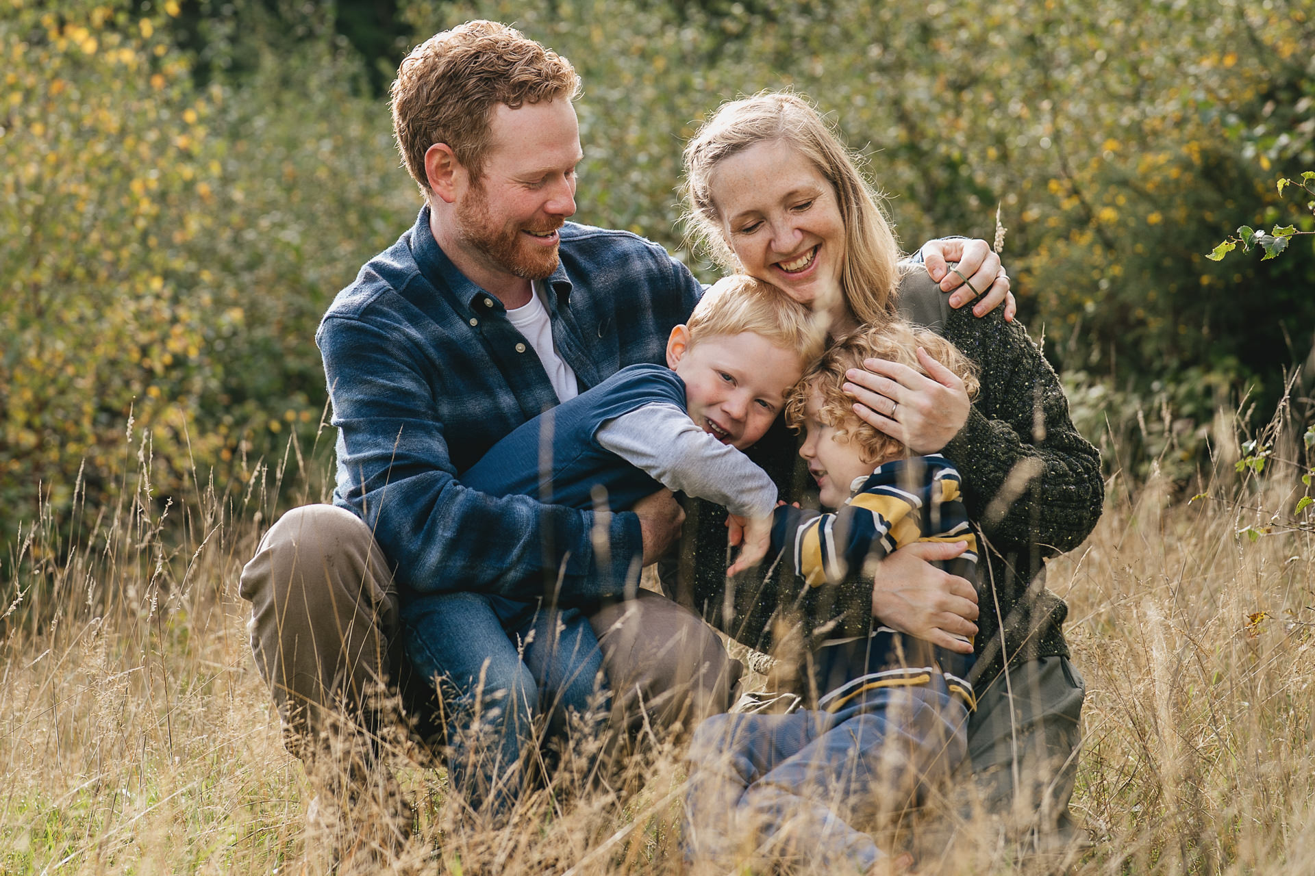 Parents with two young children cuddling and laughing together in a woodland setting