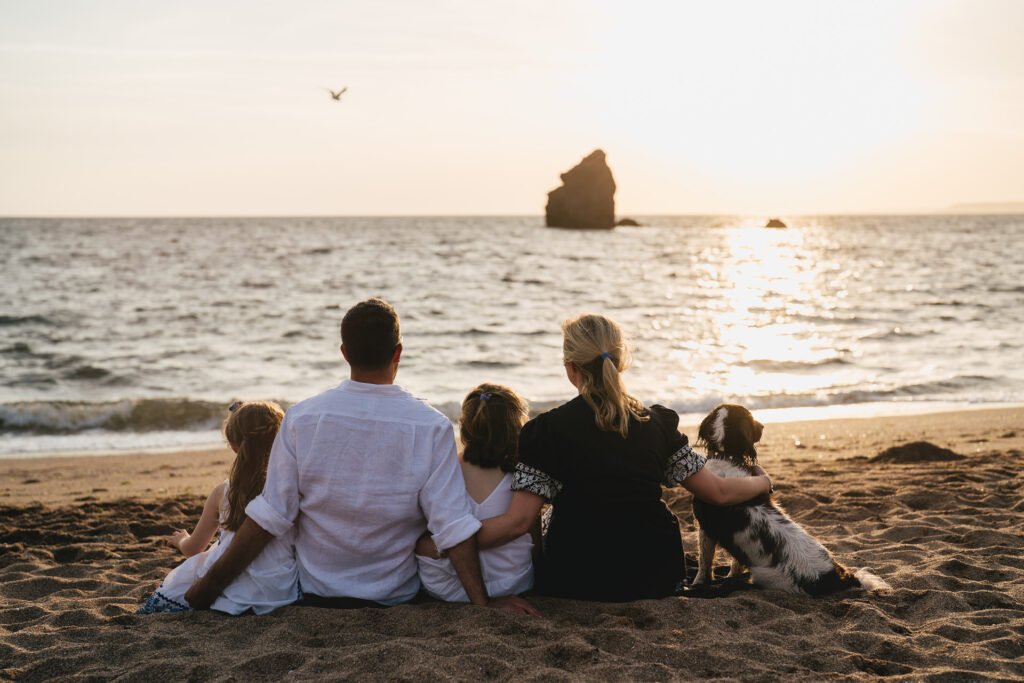 A family sitting arm in arm on the beach together at sunset and looking out to sea