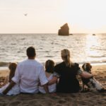 A family sitting arm in arm on the beach together at sunset and looking out to sea