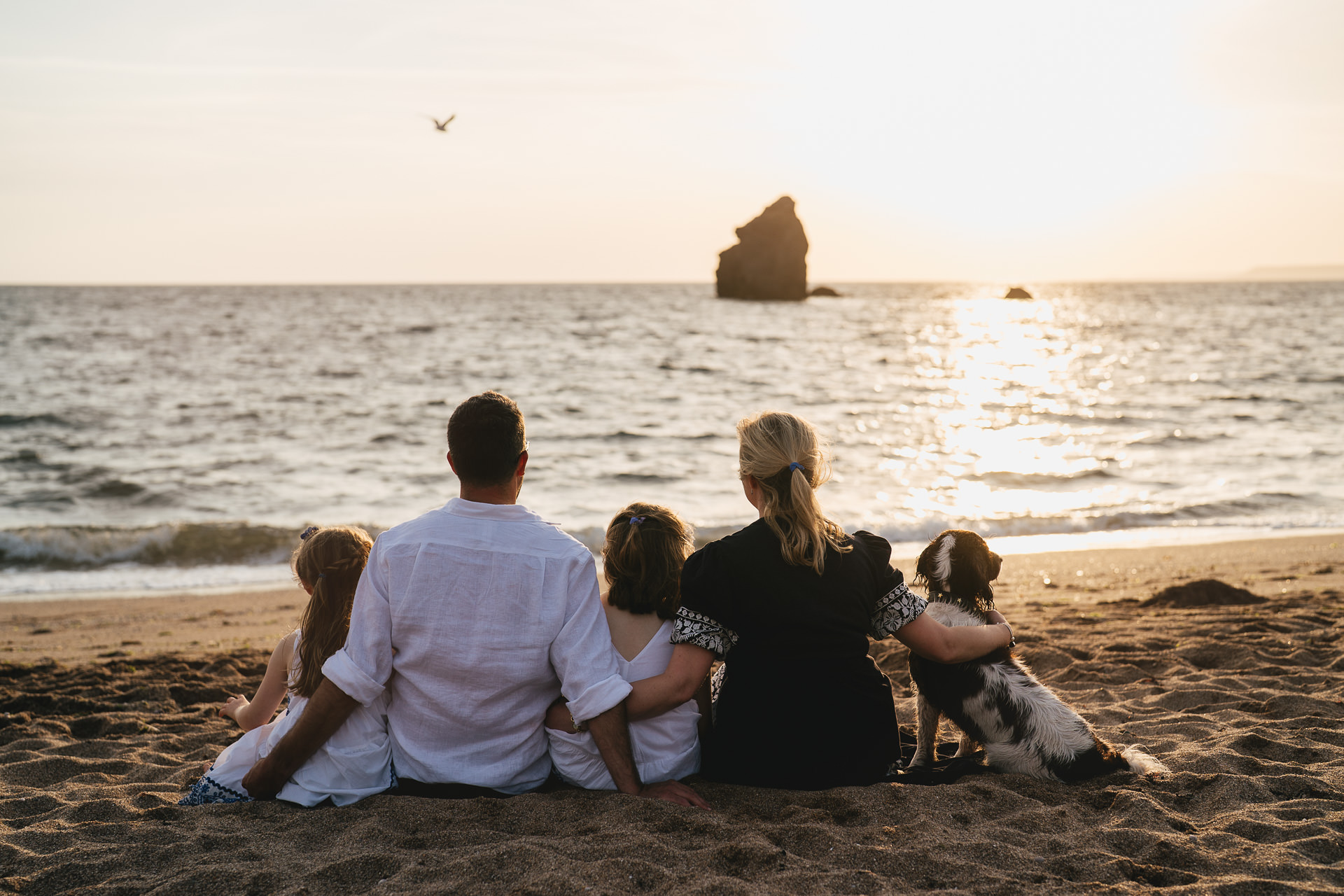 A family sitting arm in arm on the beach together at sunset and looking out to sea