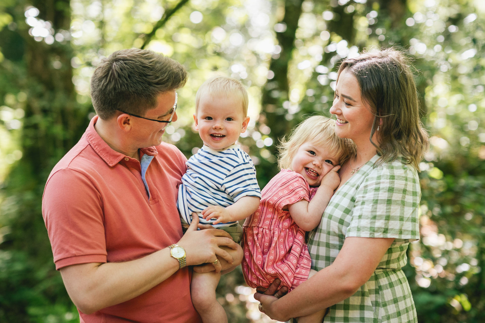 Parents cuddling twin toddlers in woodland in Devon. 