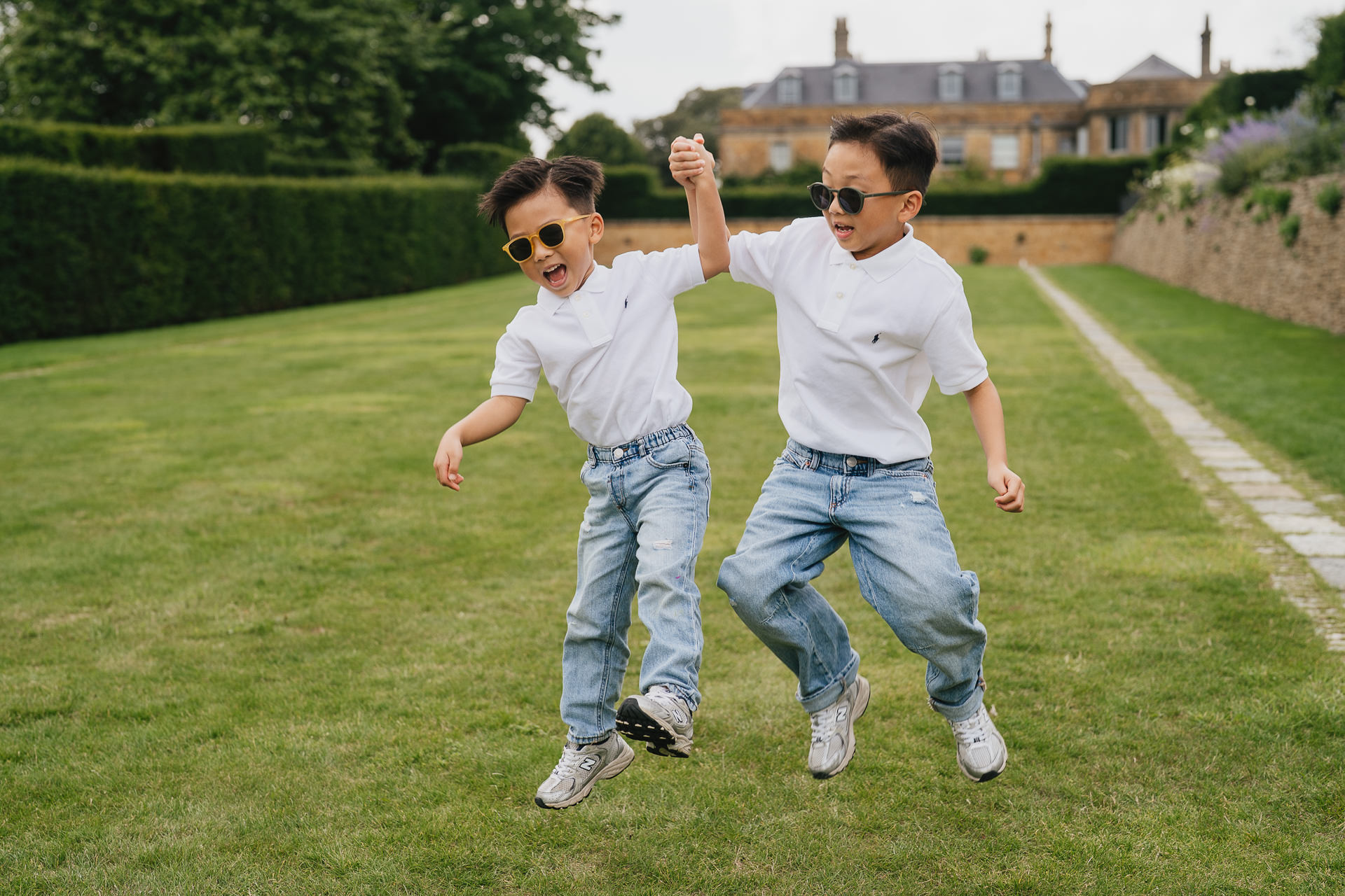 Two young brothers wearing sunglasses and jumping in the air together during a family photography session at the Newt in Somerset