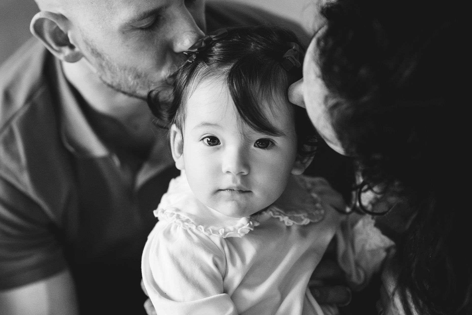 Mother and father kissing a young girl, who is looking at the camera. 