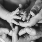 Tiny newborn fingers with adult hands underneath