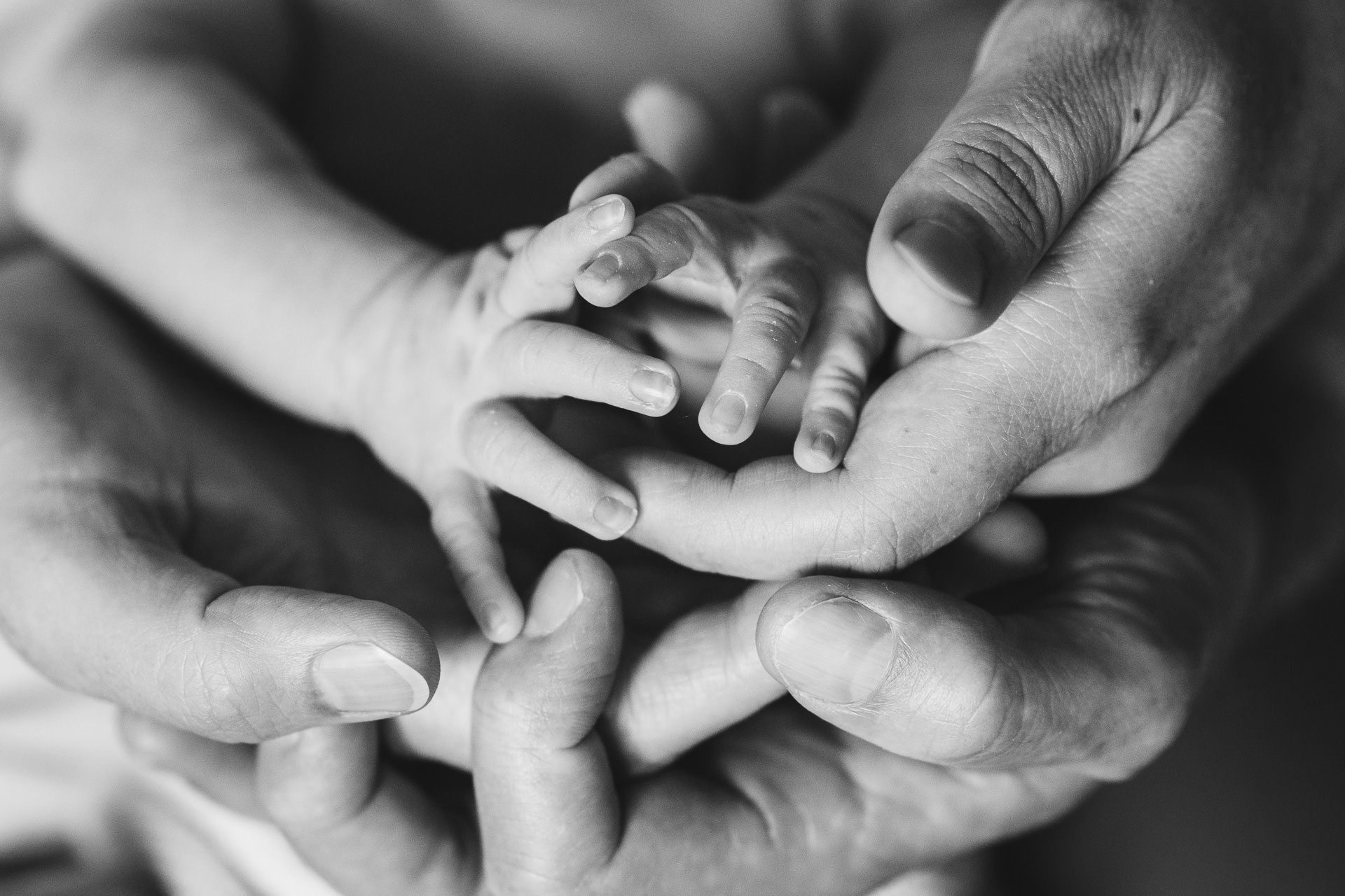 Tiny newborn fingers with adult hands underneath 