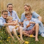 A relaxed family group photo from an extended family photography session in Devon with parents sitting amongst long grass with three boys