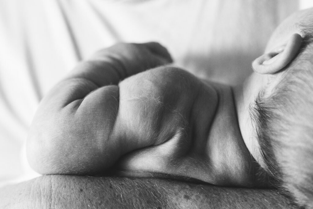 A close up photo from a newborn photography session, of a baby's shoulder and arm, with scrunched up baggy skin and fluffy hair.