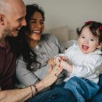 A baby girl laughing and playing with her parents on their bed for an at home photography session
