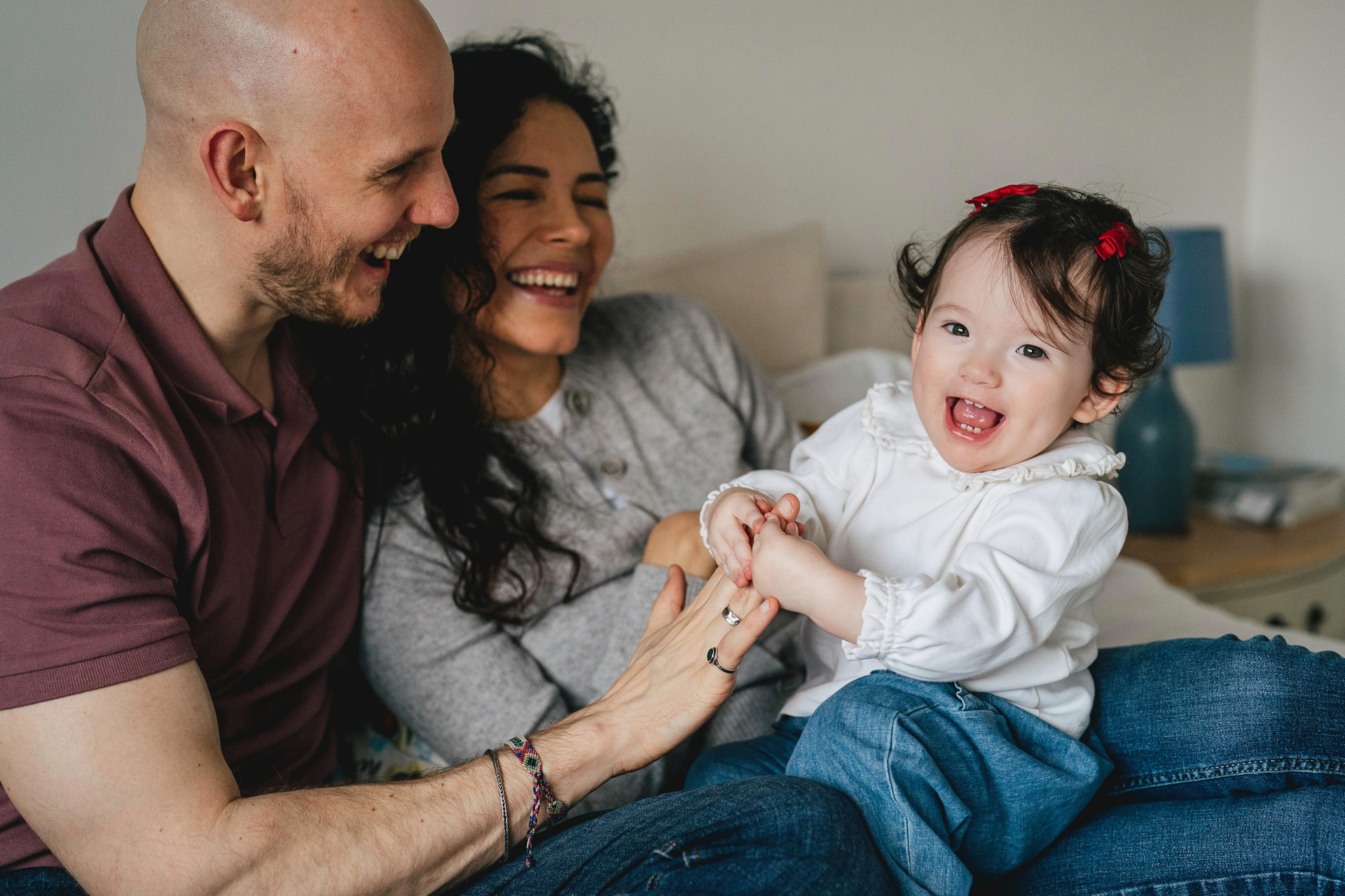 A baby girl laughing and playing with her parents on their bed for an at home photography session