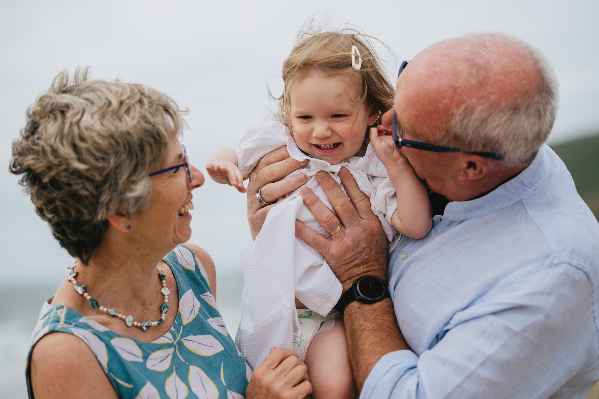 Grandparents playing with their granddaughter in arms at the beach in North Devon