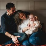 Parents with a smiling baby girl, sitting on their bed together in North Devon