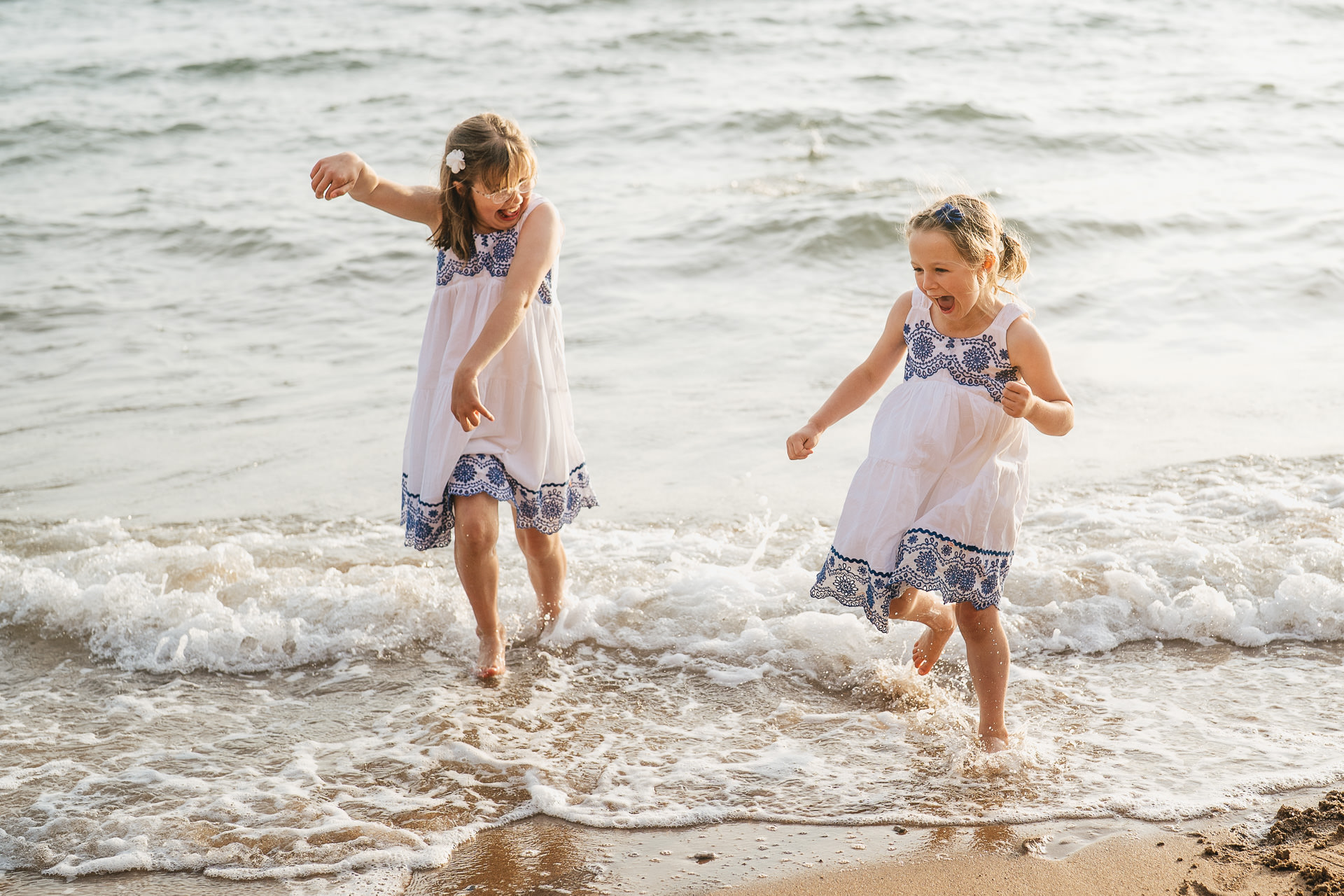 Two sisters in white dresses playing in the sea together on holiday in Devon