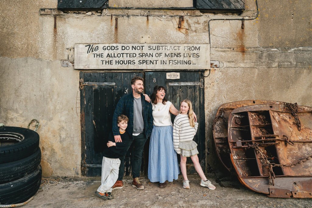 A family group photo in Lyme Regis with a relaxed and smiling family standing by some fishing crates in front of a black painted door
