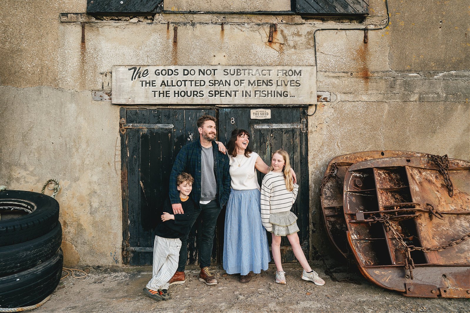 A family group photo in Lyme Regis with a relaxed and smiling family standing by some fishing crates in front of a black painted door