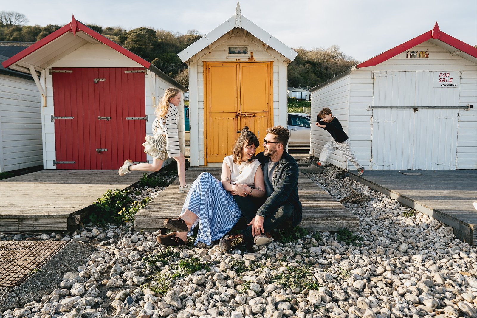 A photo of a family playing together by the beach huts in Lyme Regis, during a family photo session with Helen Lisk Photography
