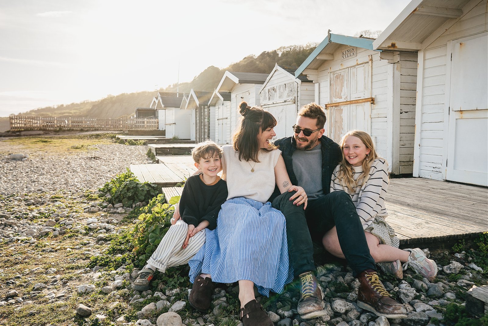 A natural family portrait sitting together by the beach huts in Lyme Regis, during a family photo session 