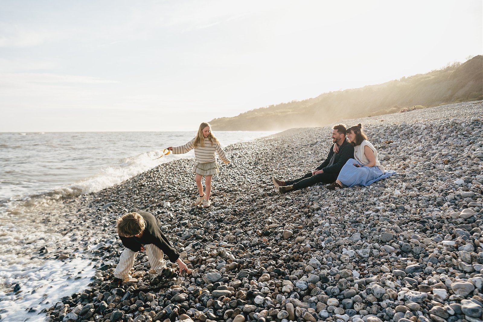 A family on Monmouth beach in Lyme Regis, during a family photography session with the sun setting