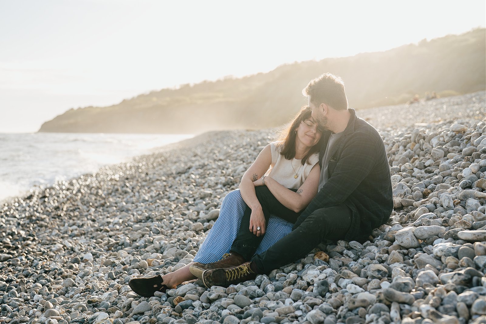 A couple cuddling together on Monmouth beach in Lyme Regis, during a family photography session with the sun setting