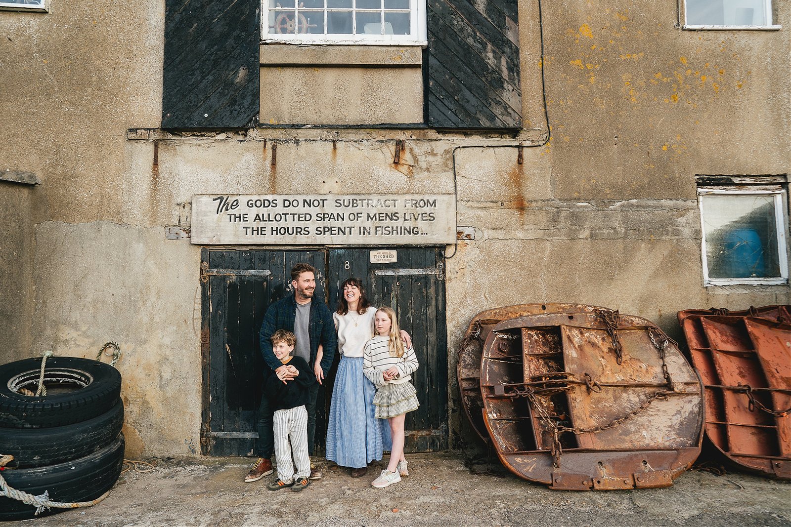 A relaxed family photo in Lyme Regis, with the family standing in front of a painted black door with fishing nets close by