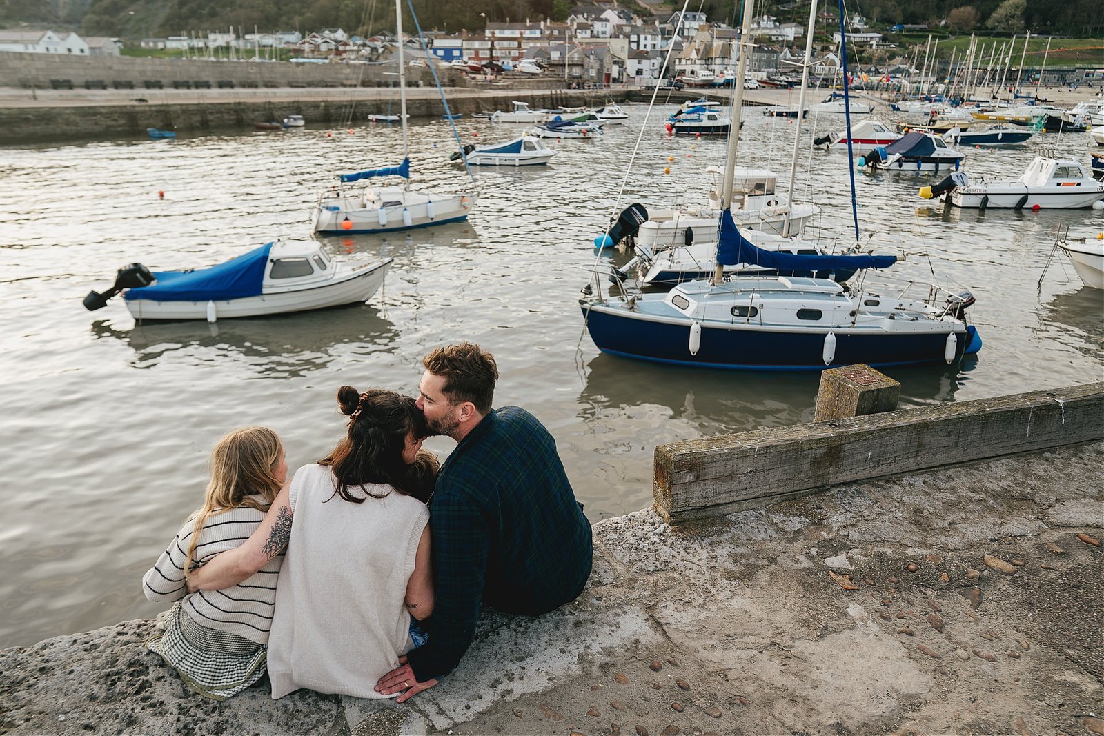 A family sitting together at the end of their photography session, looking across Lyme Regis harbour and cuddling together