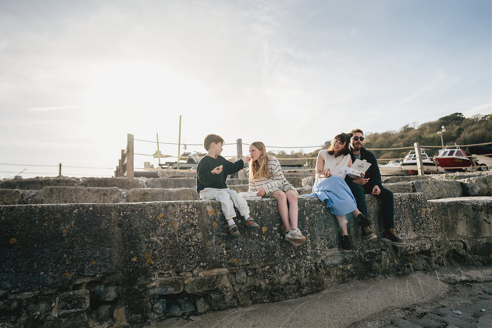 Parents with two children sitting on the Cobb eating fish & chips in Lyme Regis during a family photography session