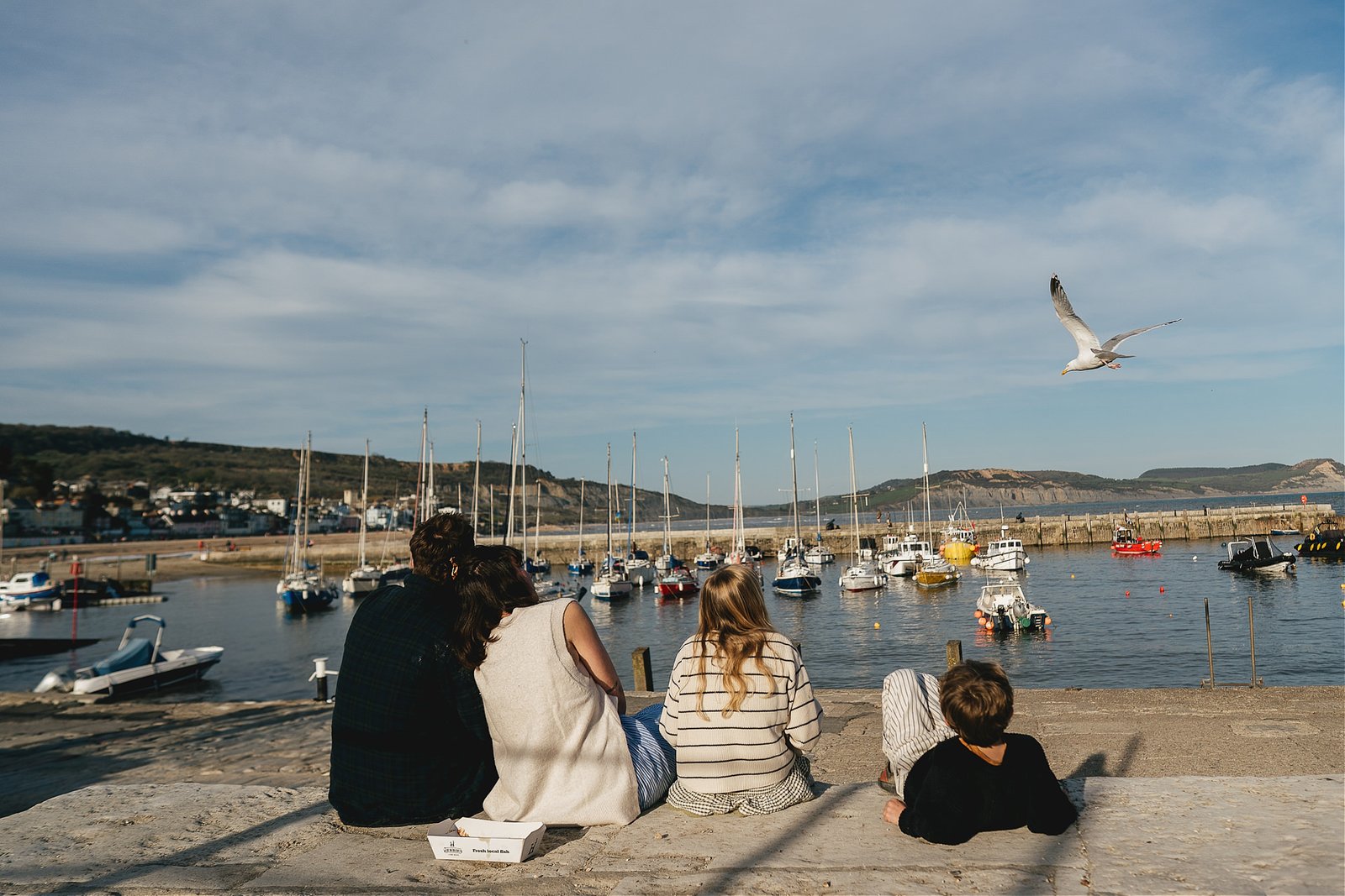 A family sitting by the harbour in Lyme Regis during a family photography session